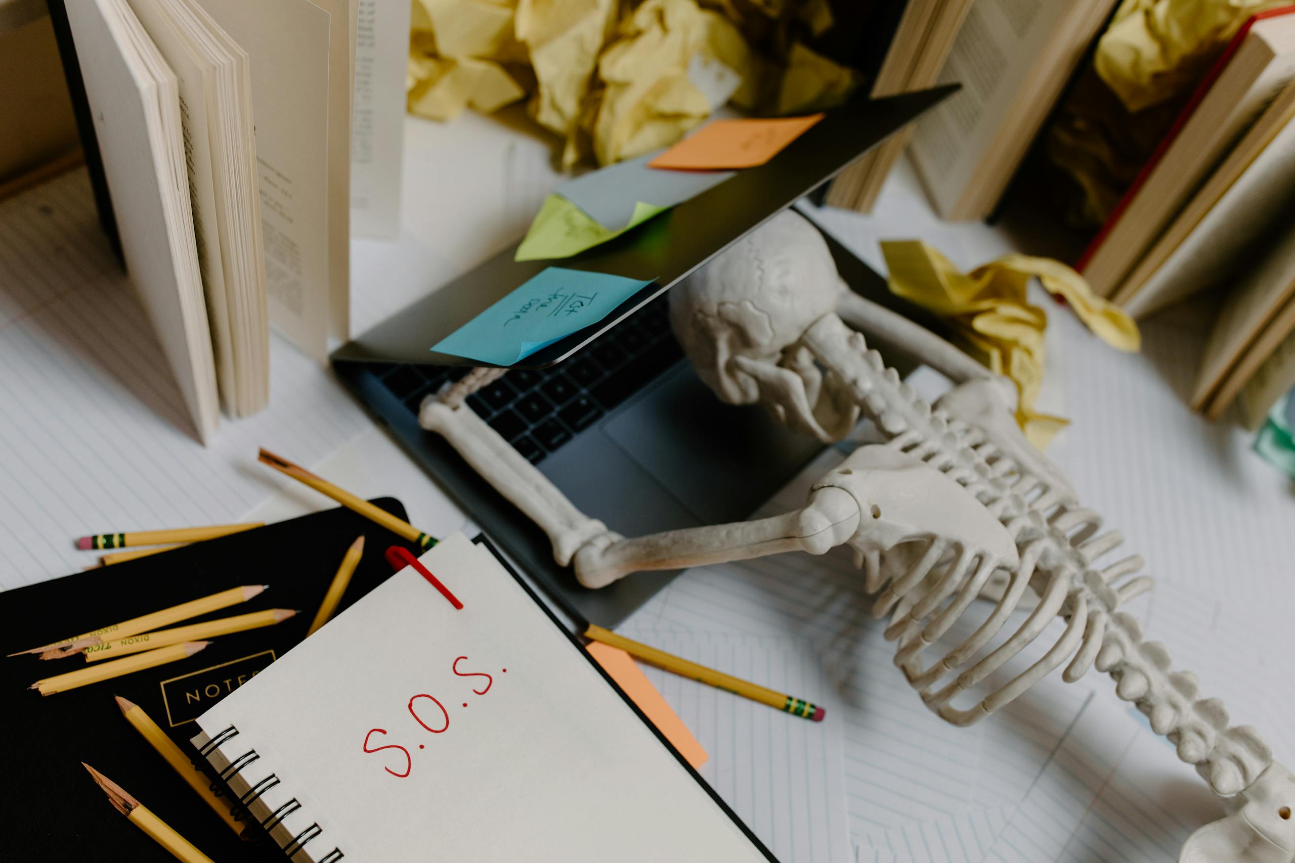 Dramatic still life of a skeleton overwhelmed at an untidy office desk with S.O.S. note.